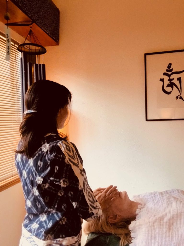 Evolene giving a Reiki treatment, hands resting gently on the patient's head